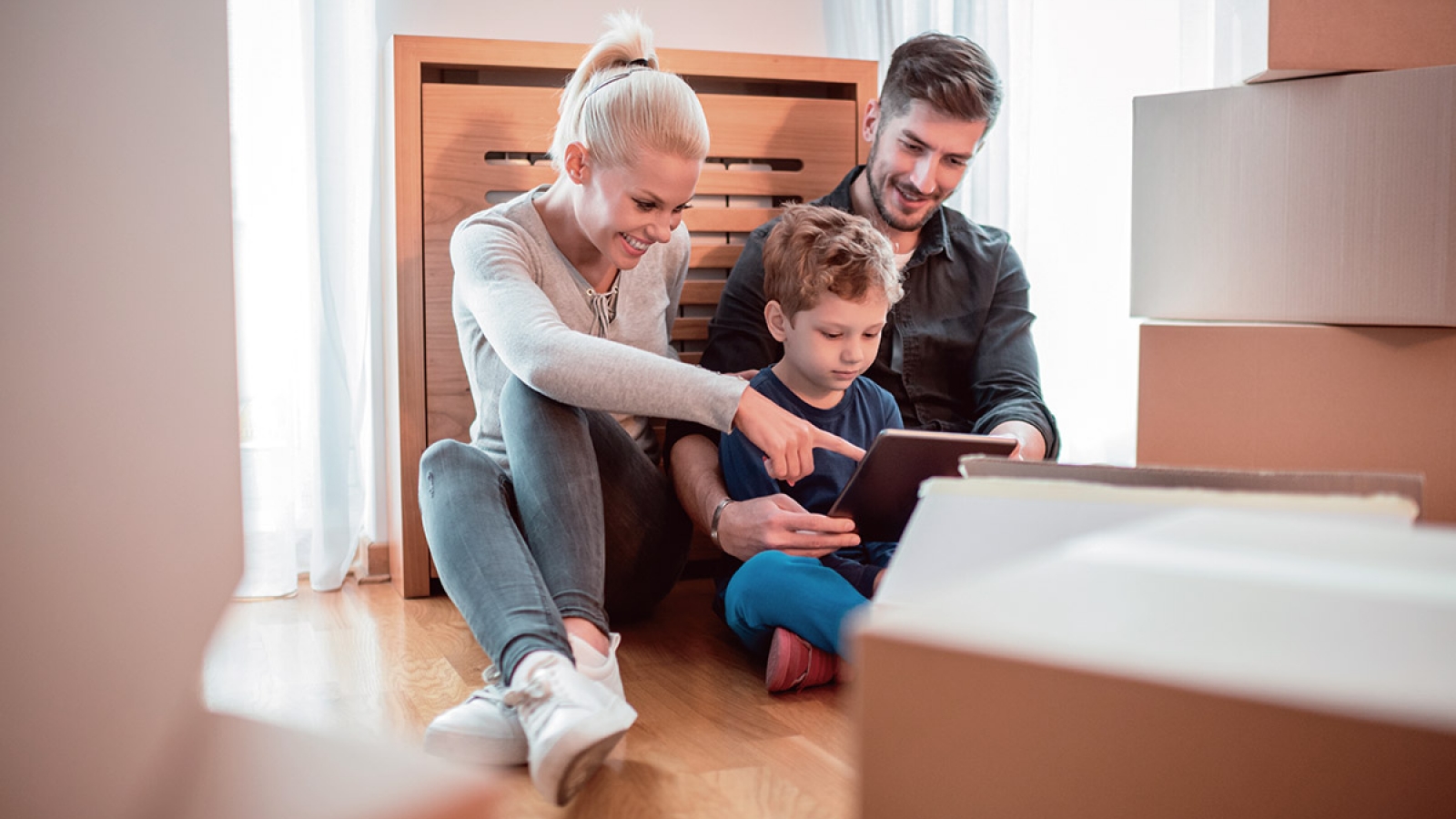 a family sitting on a hardwood floor with boxes around looking at a tablet