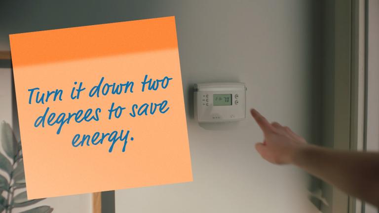 hand near thermostat turn it down two degrees to save energy