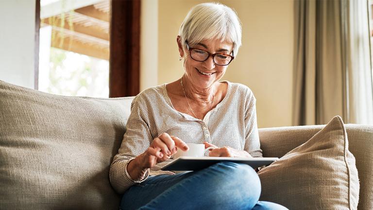 older woman sitting on a couch with coffee and iPad